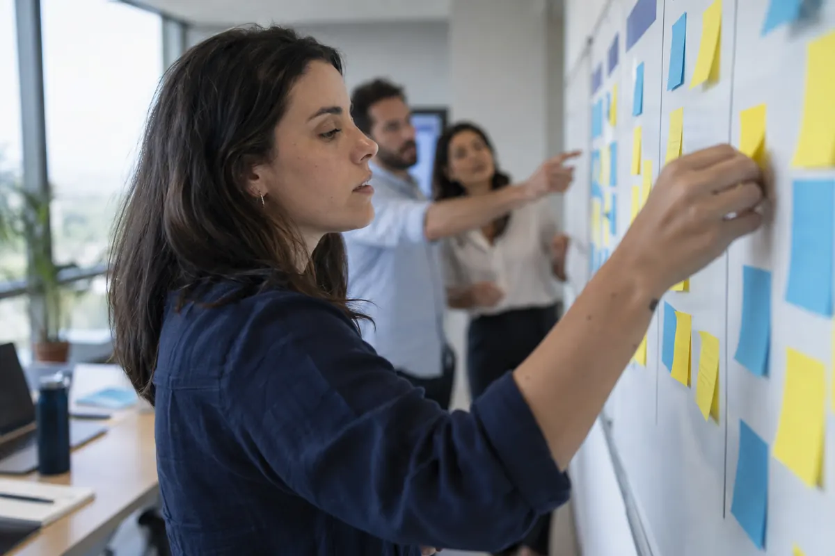 Mão colando um post-it no quadro enquanto a equipe discute as exceções do fluxo